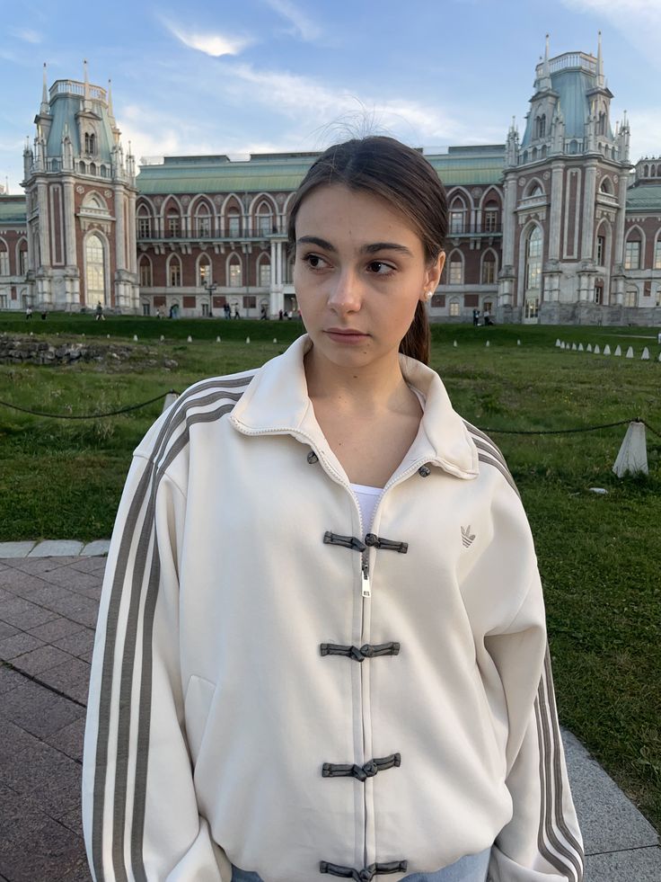 Person wearing a cream-colored white-cny-jacket with black buttons and stripes in front of an ornate building.
